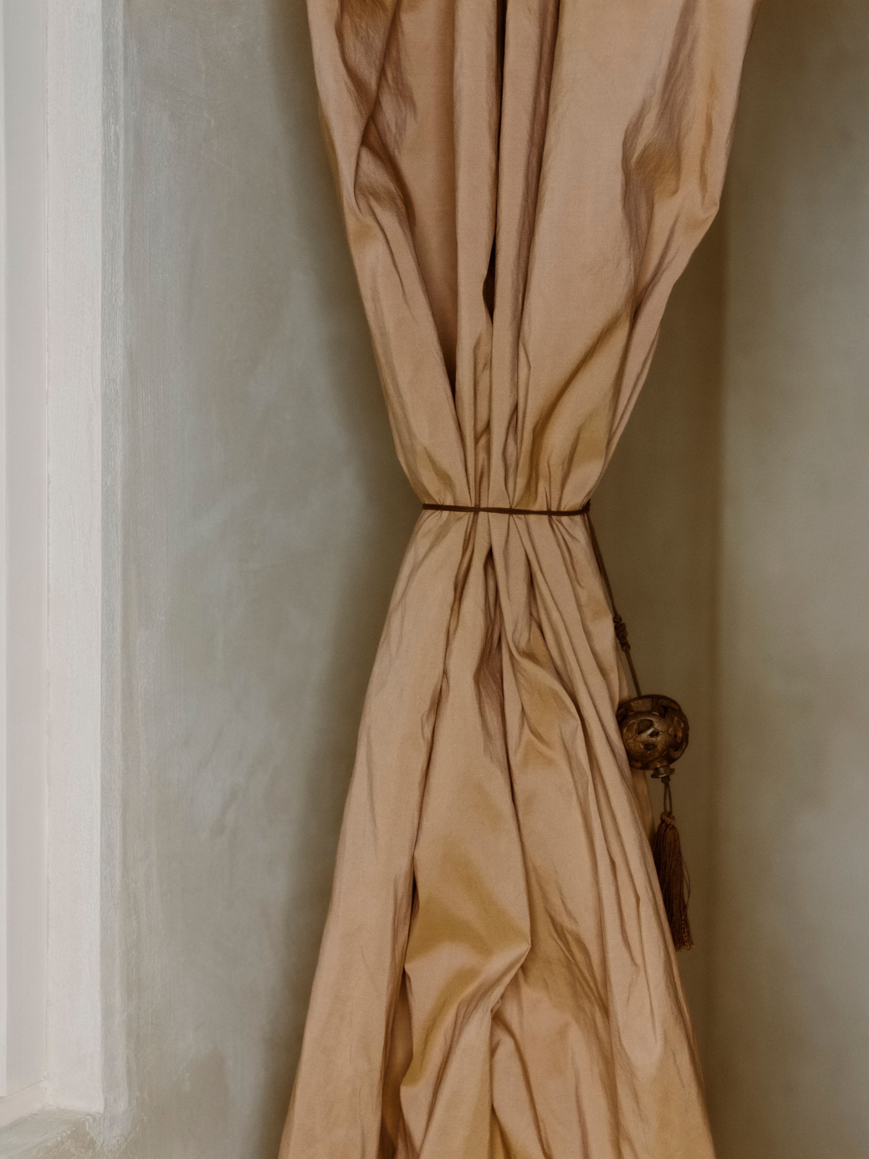 a gathered orange silk curtain against a plaster wall, WOE, Width Over Ears