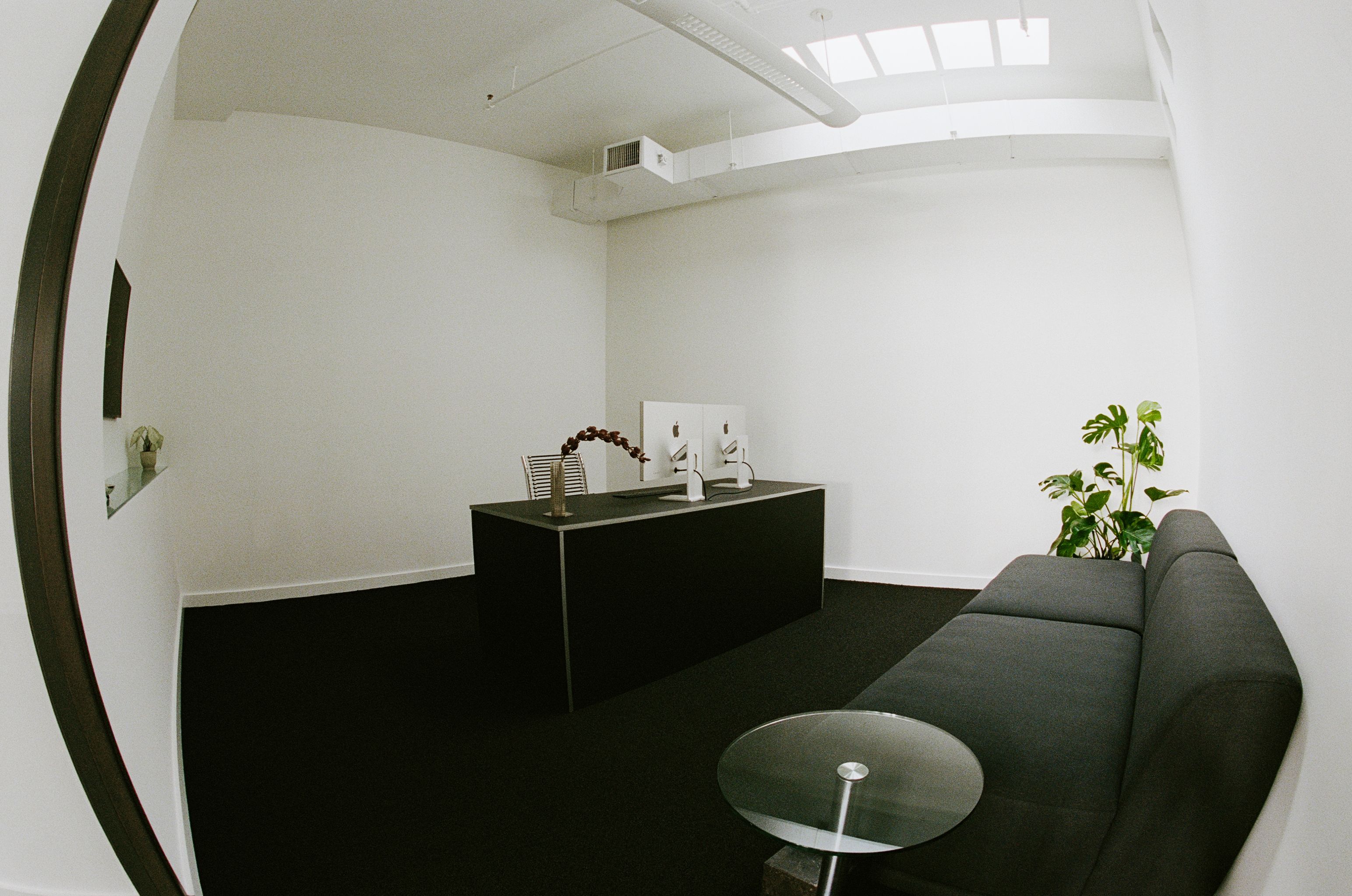 an office room with glass side table, upholstered sofa, and black desk