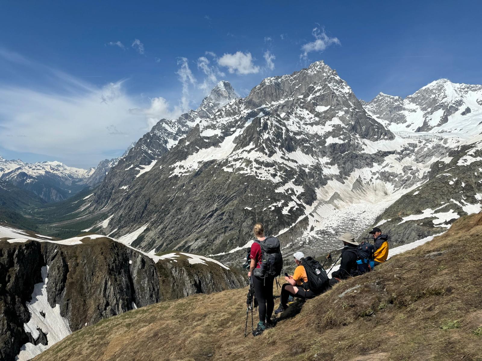Integrantes del grupo hacen una pausa en una ladera frente a montañas nevadas.