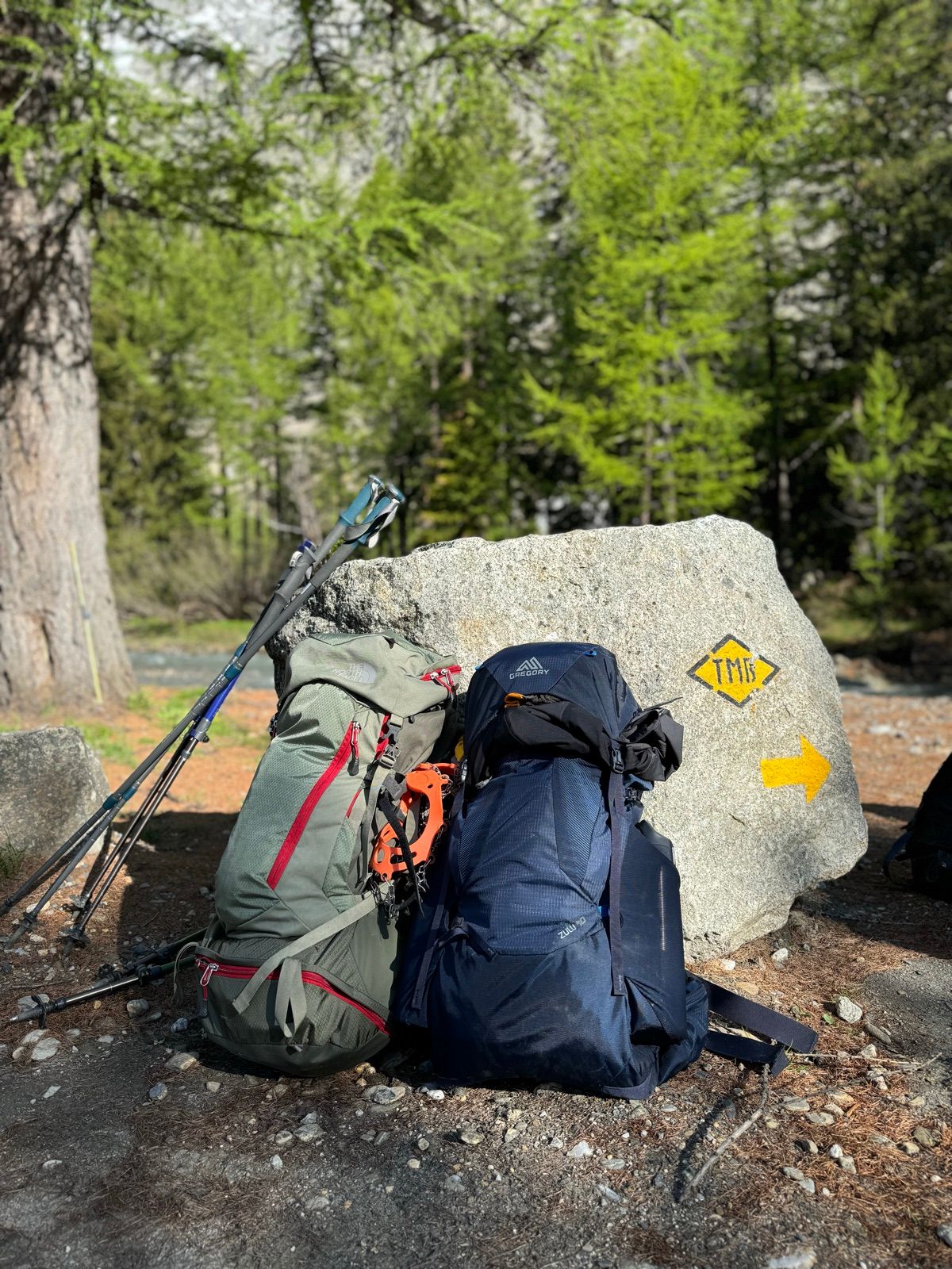 Dos mochilas, bastones y crampones apoyados en una roca con la señal amarilla del Tour du Mont Blanc