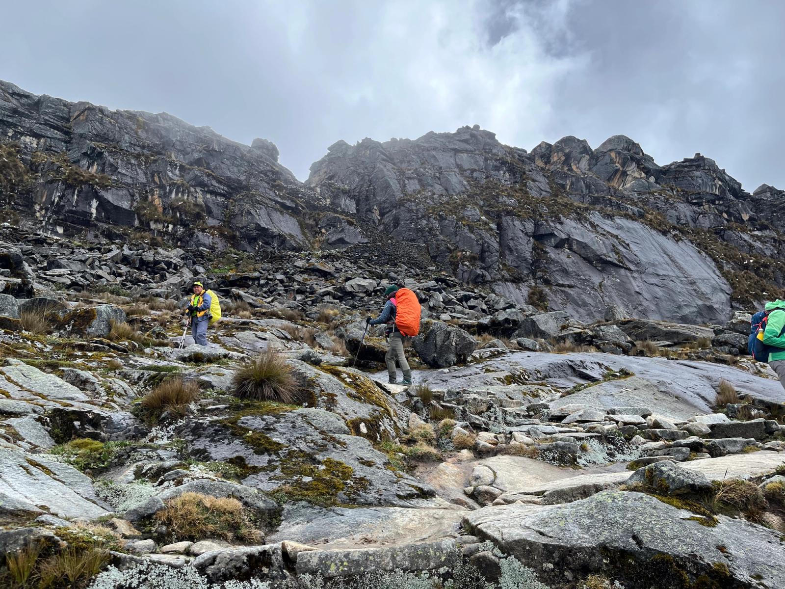 Guía y excursionistas con mochilas y bastones avanzan entre rocas hacia el paso Punta Unión, bajo un cielo nublado.