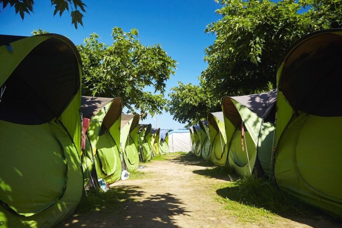 Row of bright green dome tents lining a shaded dirt path under trees at a campground on a clear day.