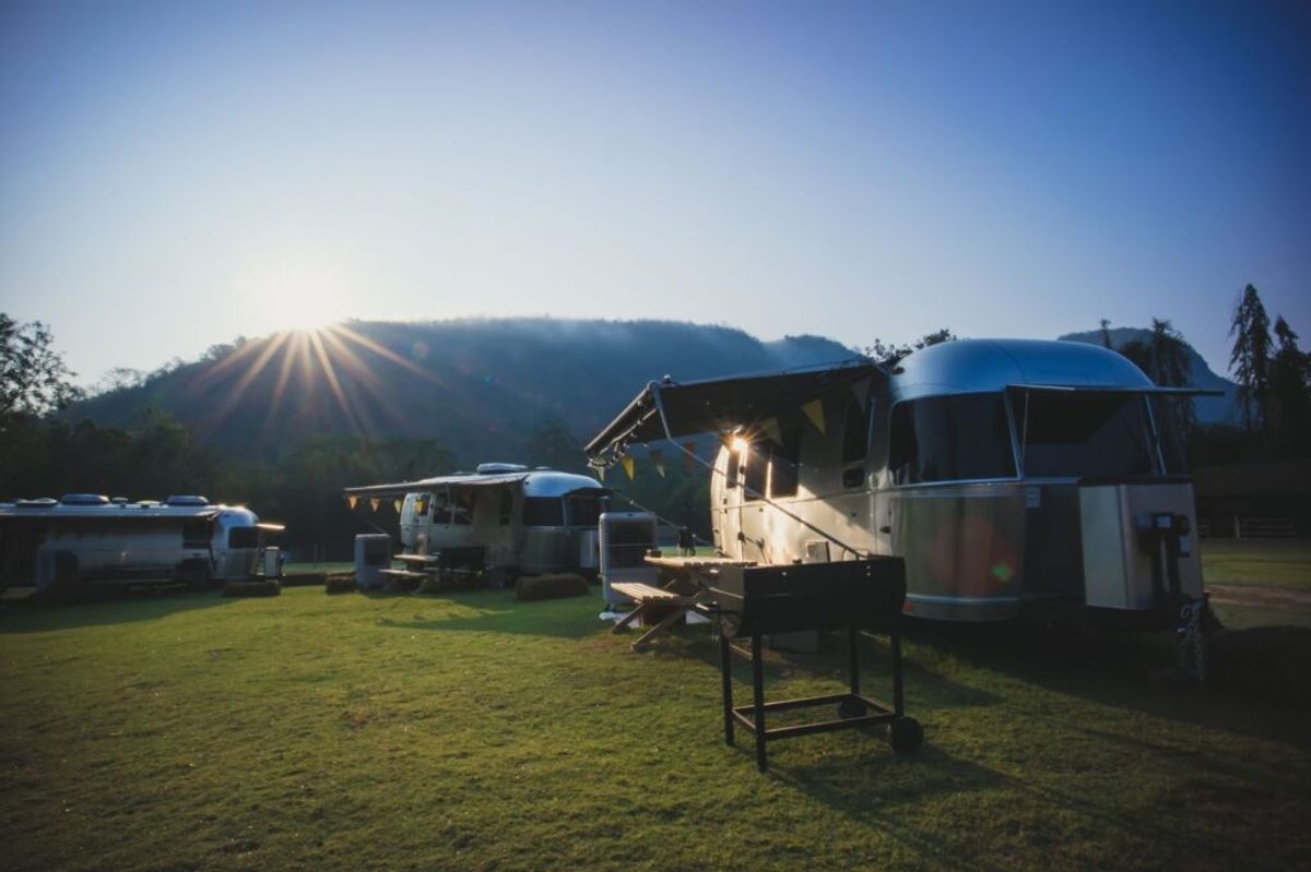 Multiple silver Airstream trailers parked on a grassy field at sunrise with forested mountains in the background.