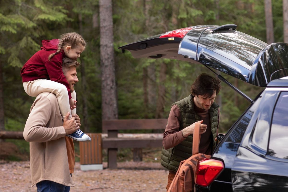 Family of four loading luggage into parked SUV at forest campground with tall pine trees in background.