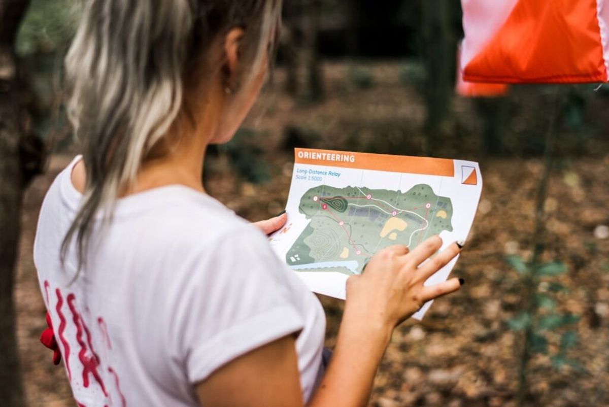 Person holding an orienteering map during a long-distance relay event outdoors, studying the course route with terrain features and checkpoints marked.