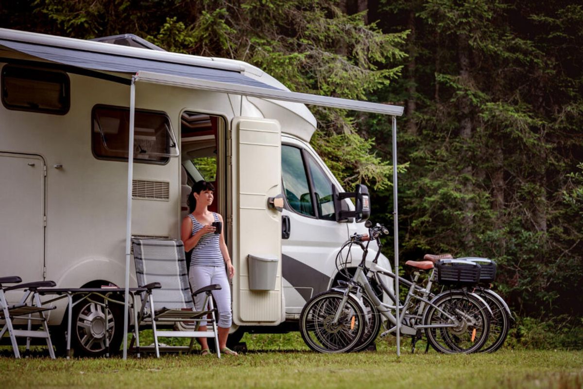 a woman drinking coffee outside of her camper van in a RV park