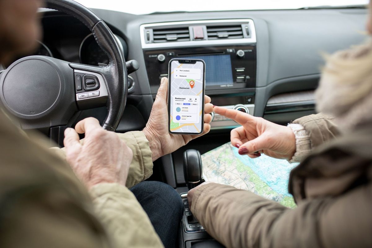 Two people in a car reviewing a restaurant location on a smartphone and paper map during a road trip.