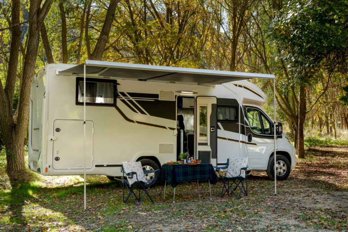 A white and grey camper van in nature with two chairs and a table set up