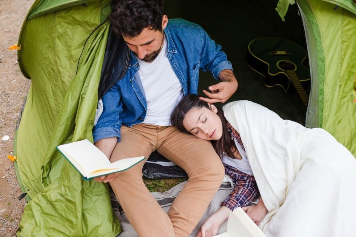 Couple relaxing inside a green tent, reading a book together while camping outdoors.