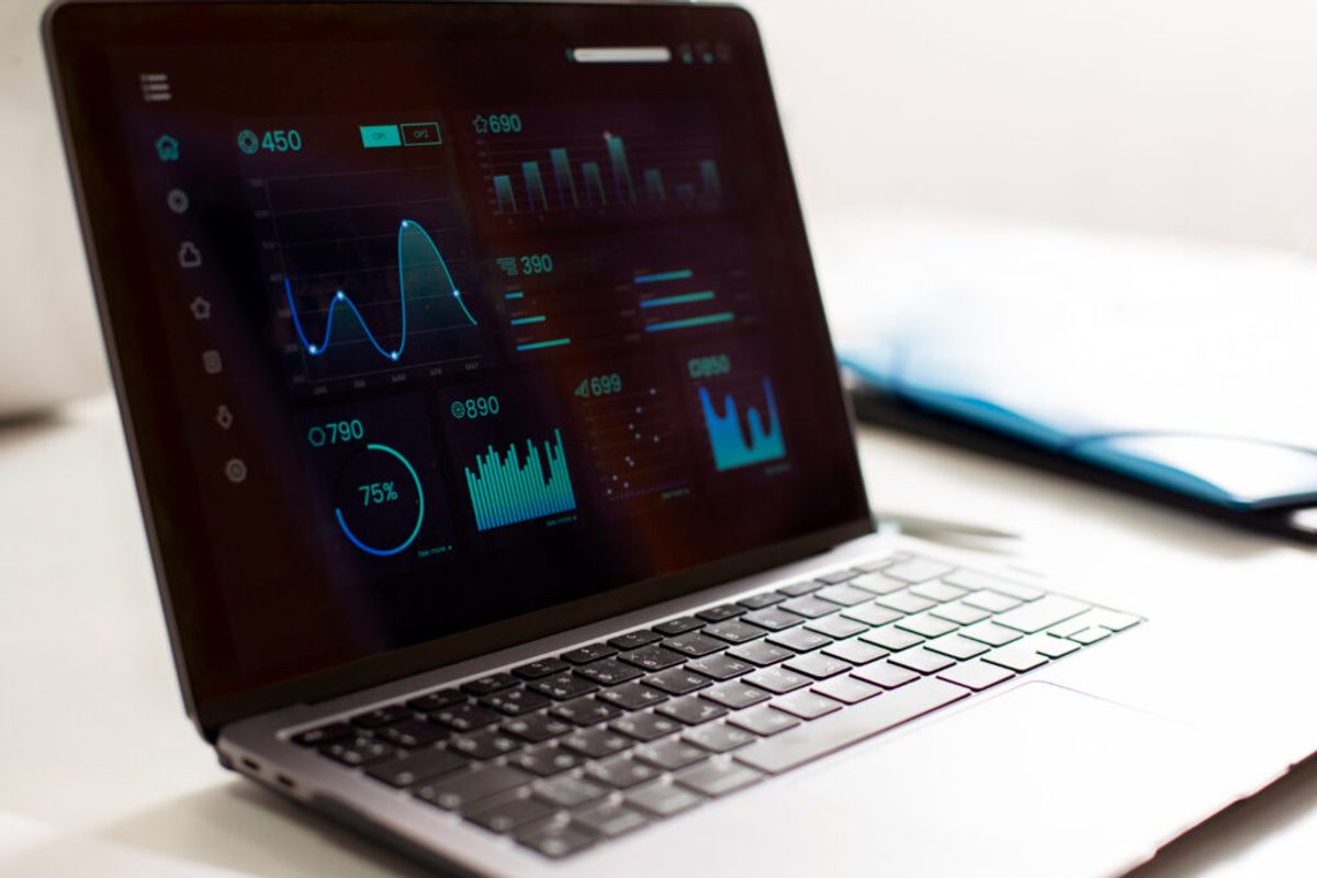Laptop displaying analytics dashboard with glowing blue and cyan charts, graphs, and numerical data metrics on dark background.