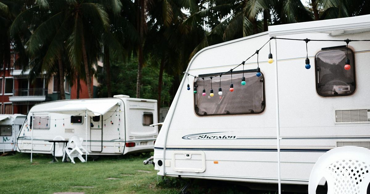 White travel trailers parked in a grassy campground with palm trees, colorful decorative balls hanging from awning above windows.