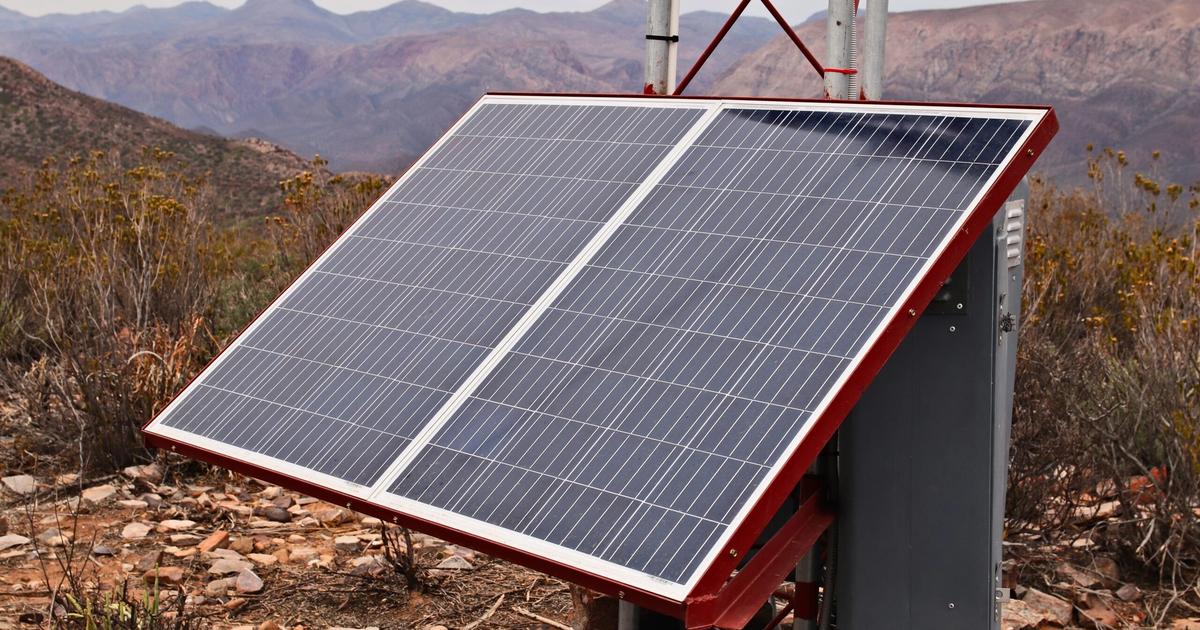 Solar panel array mounted on red frame in mountainous desert landscape, demonstrating renewable energy infrastructure for remote locations.