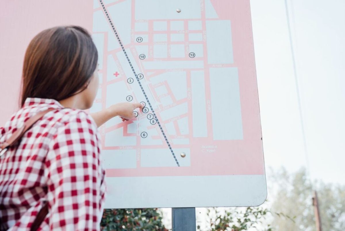 Child in red checkered shirt pointing at numbered campground map on outdoor sign.
