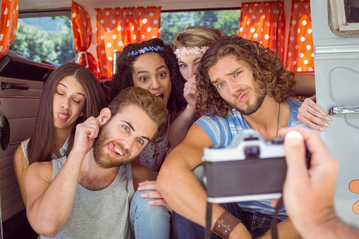 Group of young adults taking a selfie inside a camper van with red polka dot curtains and scenic views through windows.