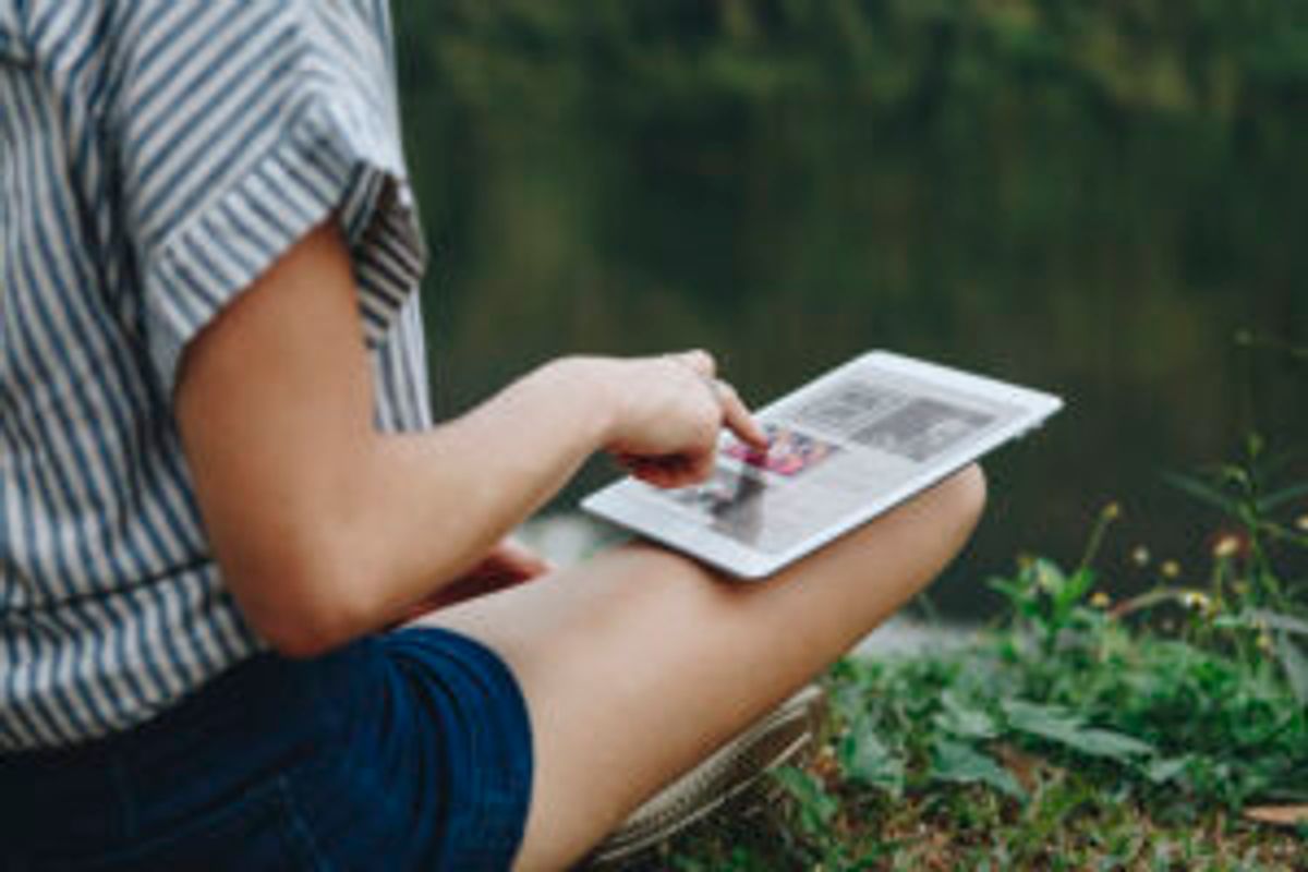 Child holding a Polaroid photo outdoors near grass, examining a printed instant photograph in natural daylight.