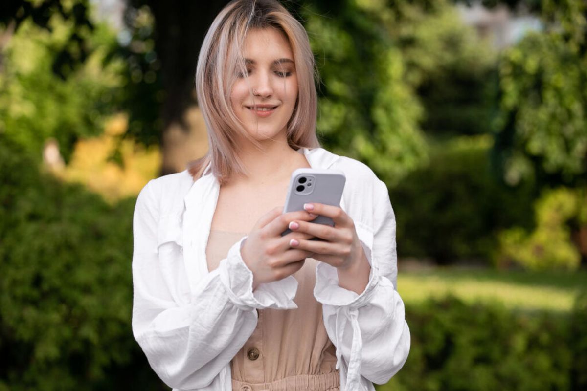 A woman in a white shirt using her phone to make a reservation using campground management software 
