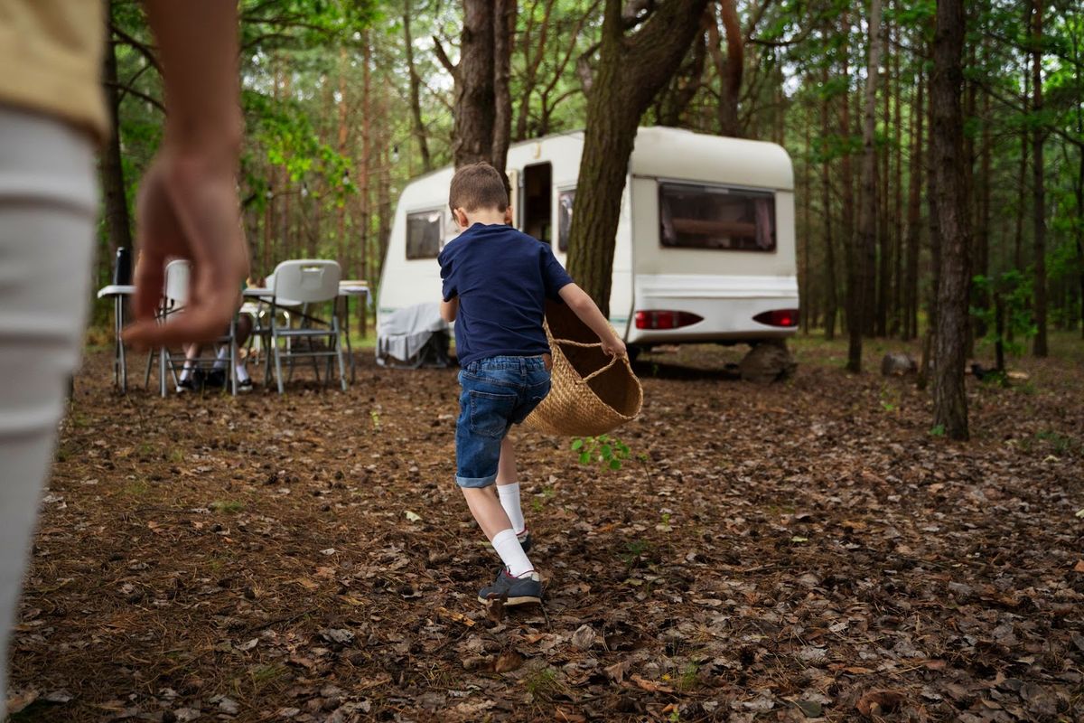 Child running with basket at campsite near RV trailer in wooded forest setting, representing family camping experience.