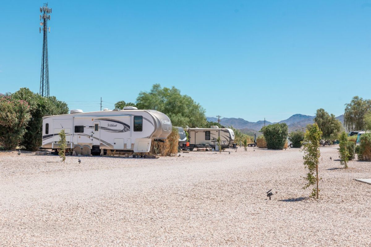 RV campground with white travel trailers parked on gravel sites, surrounded by desert landscape and mountains under clear blue sky
