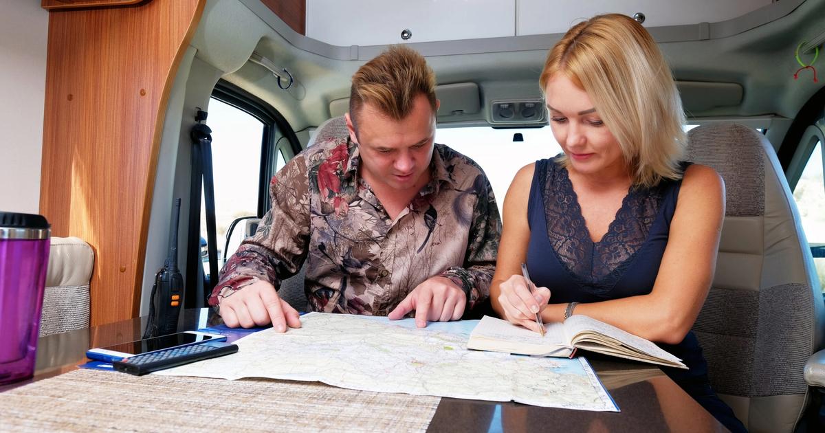 Couple inside RV reviewing map and travel guide at table, planning route for camping trip.