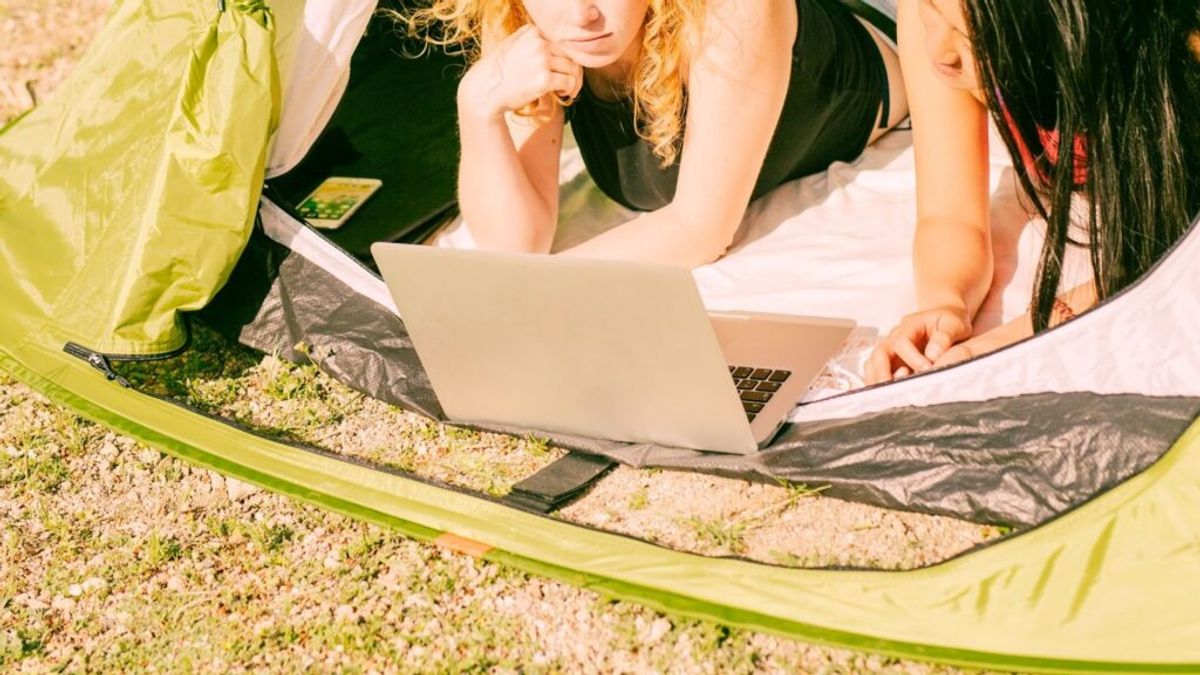 Three people inside a bright yellow tent reviewing a laptop together while sitting on sandy ground, discussing business strategy.