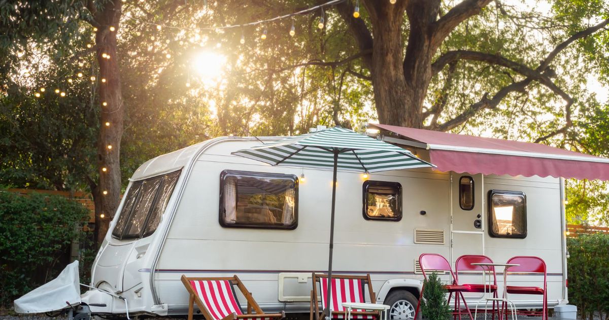 a white camper van in the forest with a beautiful sunset behing and red chairs