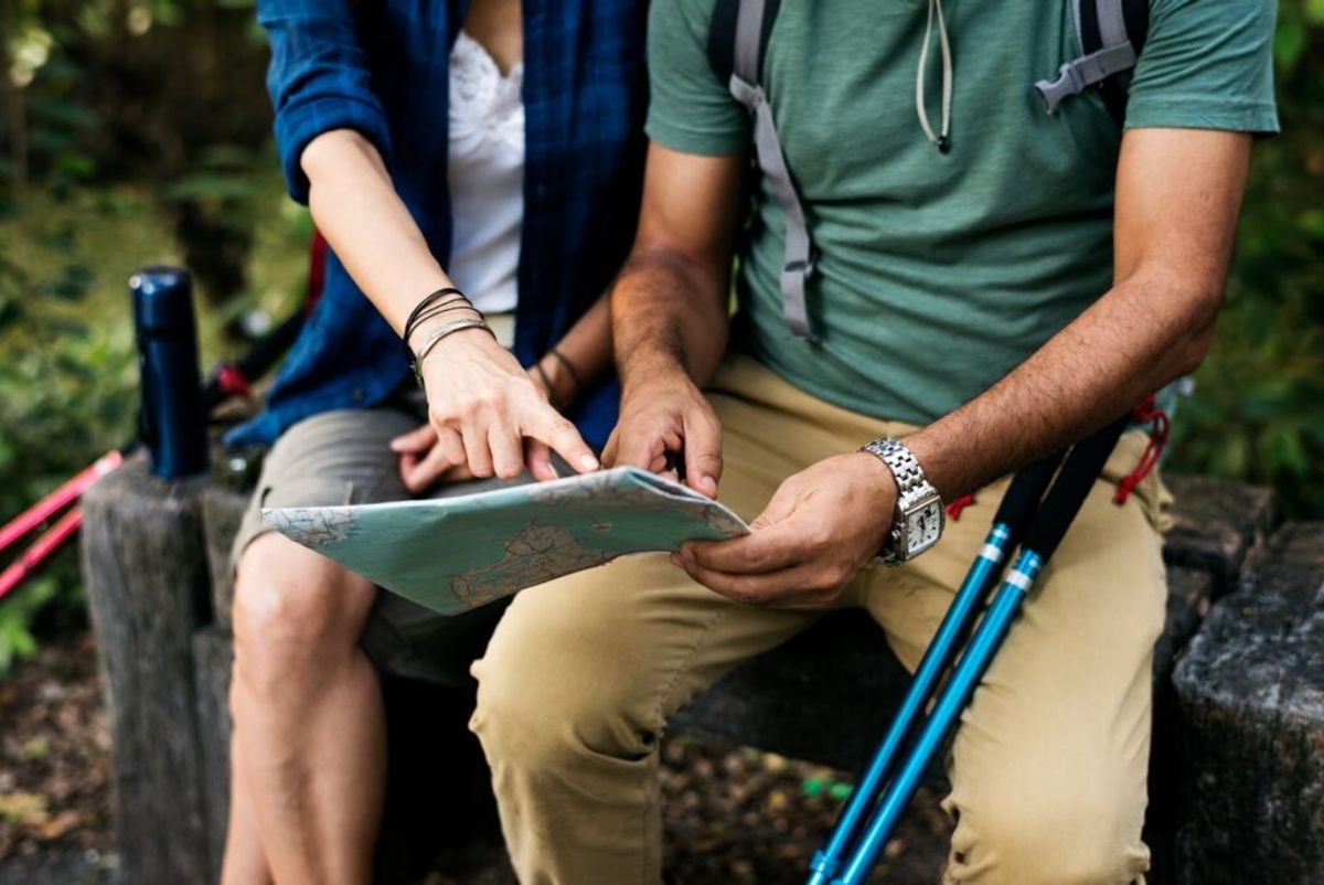Hikers with trekking poles gathered around a map during an outdoor excursion in a forested setting.