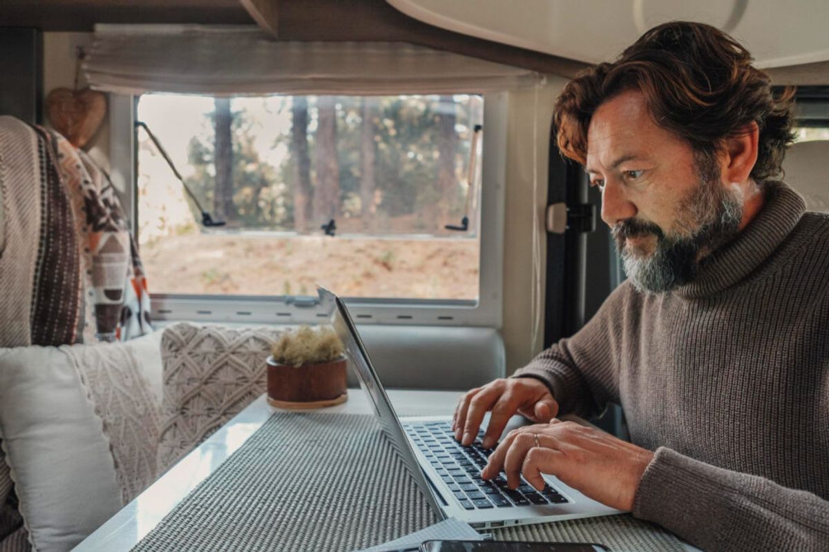 Man with a grey sueter sitting inside his camper van using a laptop to make a reservation using a campground software 