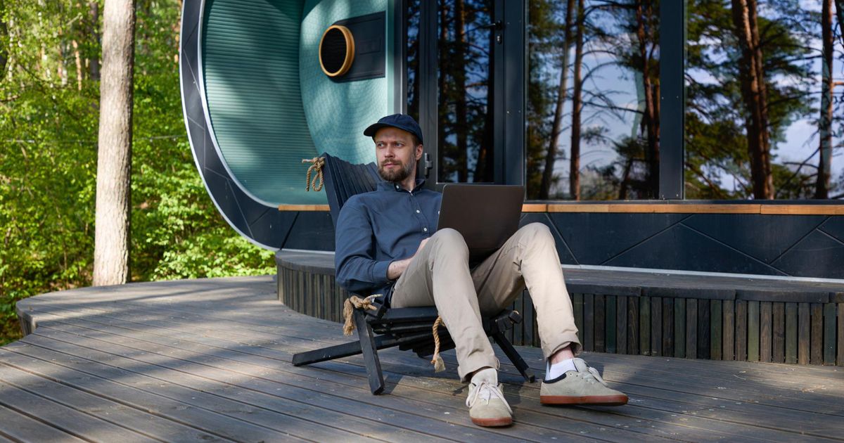 Man working on laptop in modern glamping pod with forest and lake views in background