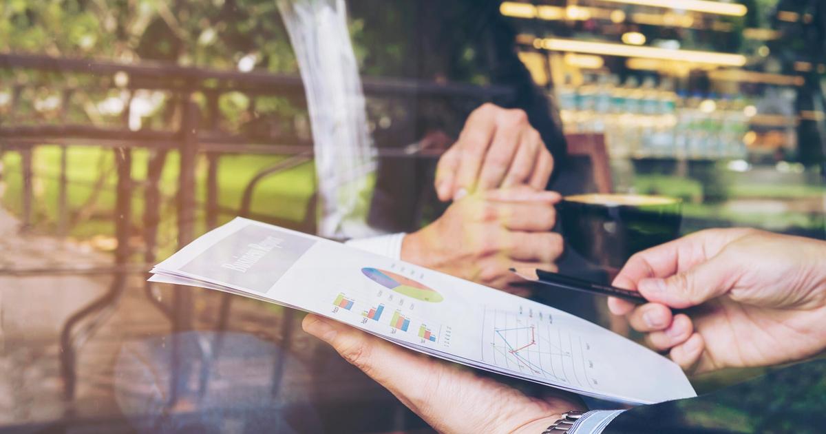 Two people reviewing financial charts and graphs on documents outdoors, analyzing data with pen and tablet for business planning.