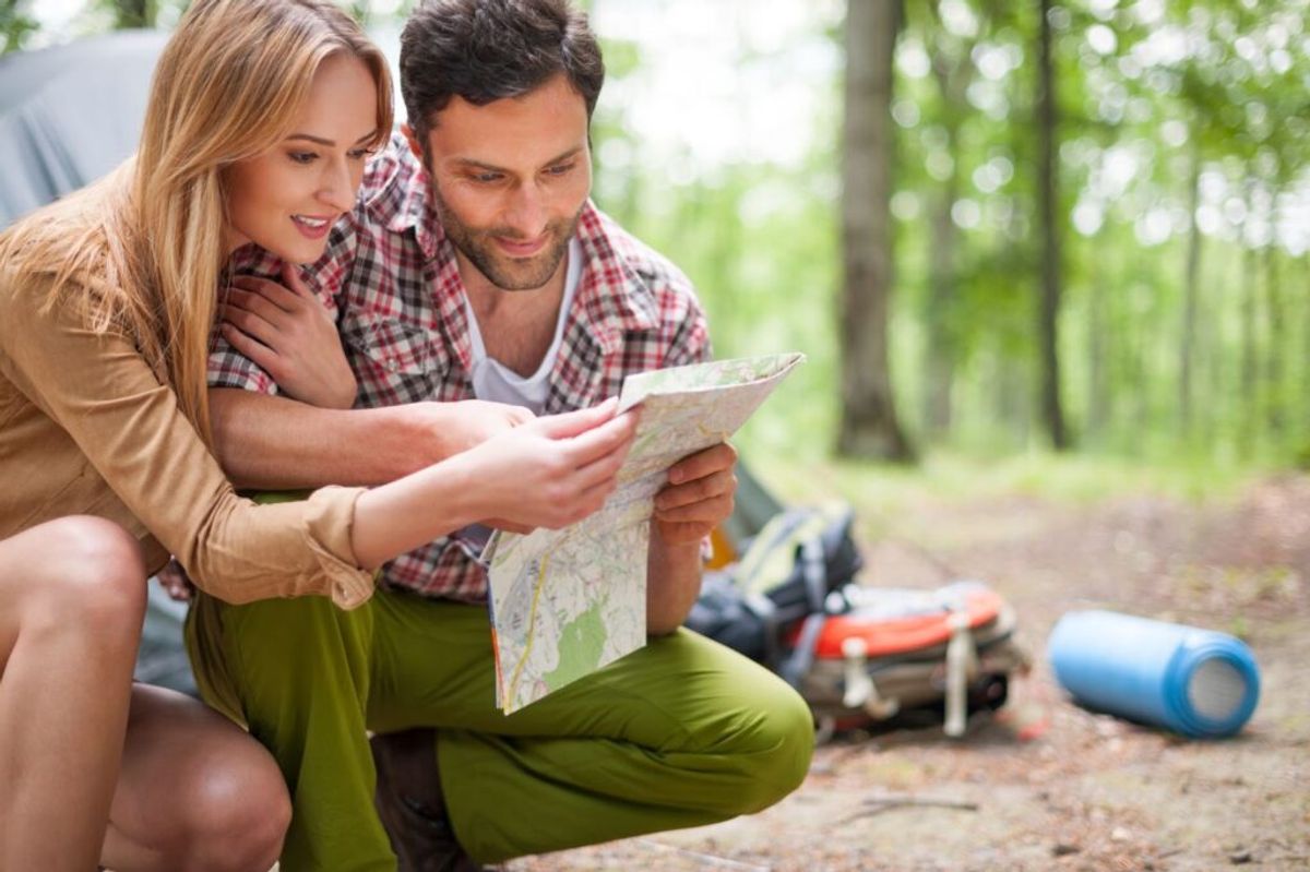 Couple reviewing a map together while camping in a forest, with camping gear visible in the background.