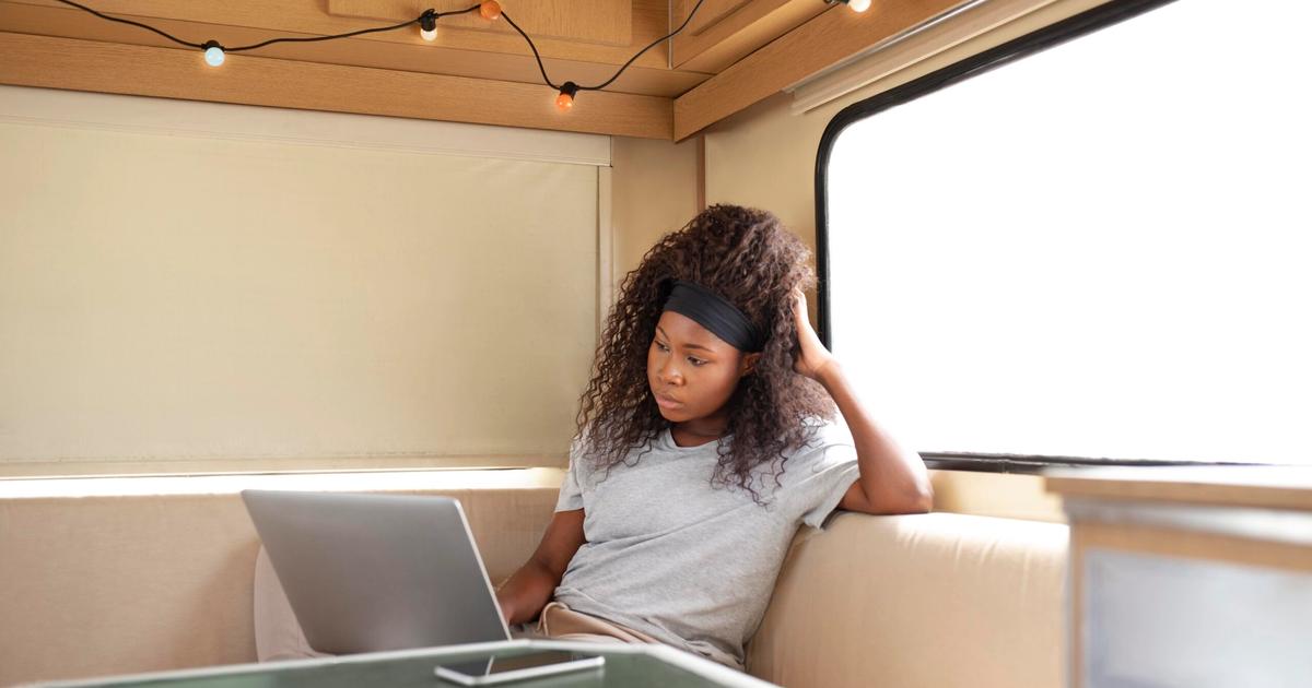 Woman working on laptop inside a modern RV with wooden ceiling and large windows, representing remote work and RV business operations.
