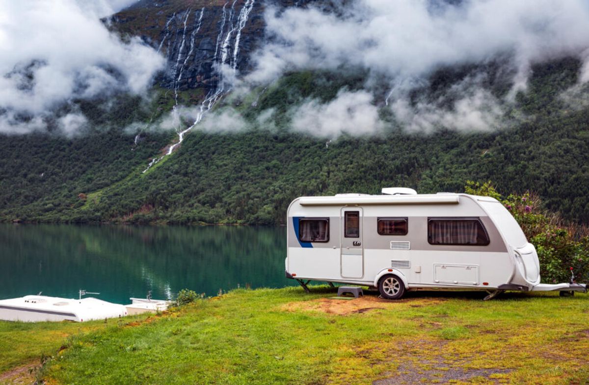 A white camper with a blue line in the mountains with the partial view of a lake