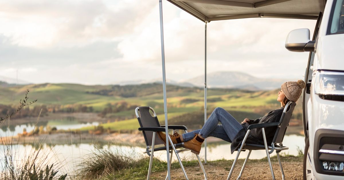 Woman with grey caridgan and jeans relaxing in front of a lake in a campground