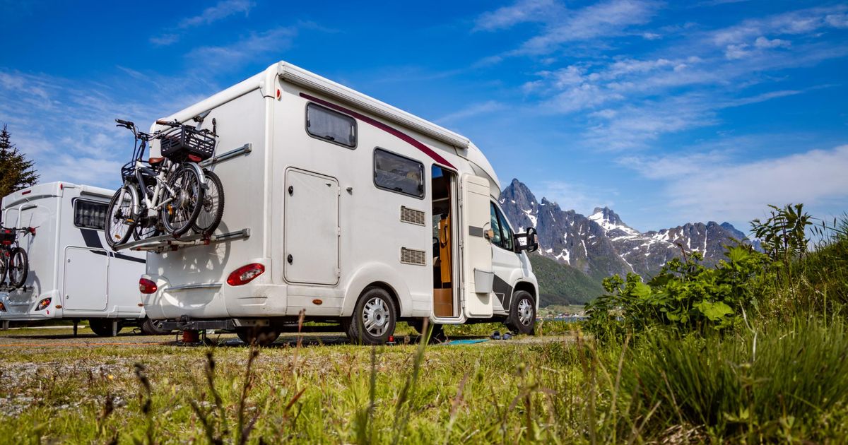 A white camper with bikes attached in the back with mountains in front of it