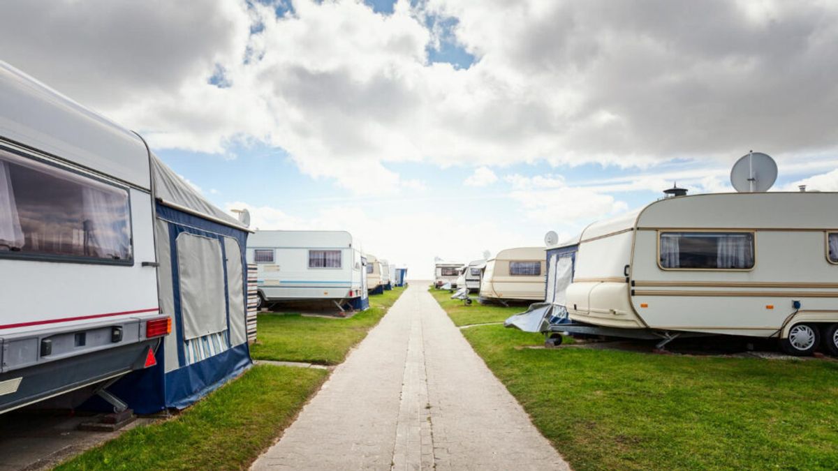 Organized caravan and RV campsite with rows of parked trailers along a paved pathway, green grass, and cloudy sky.