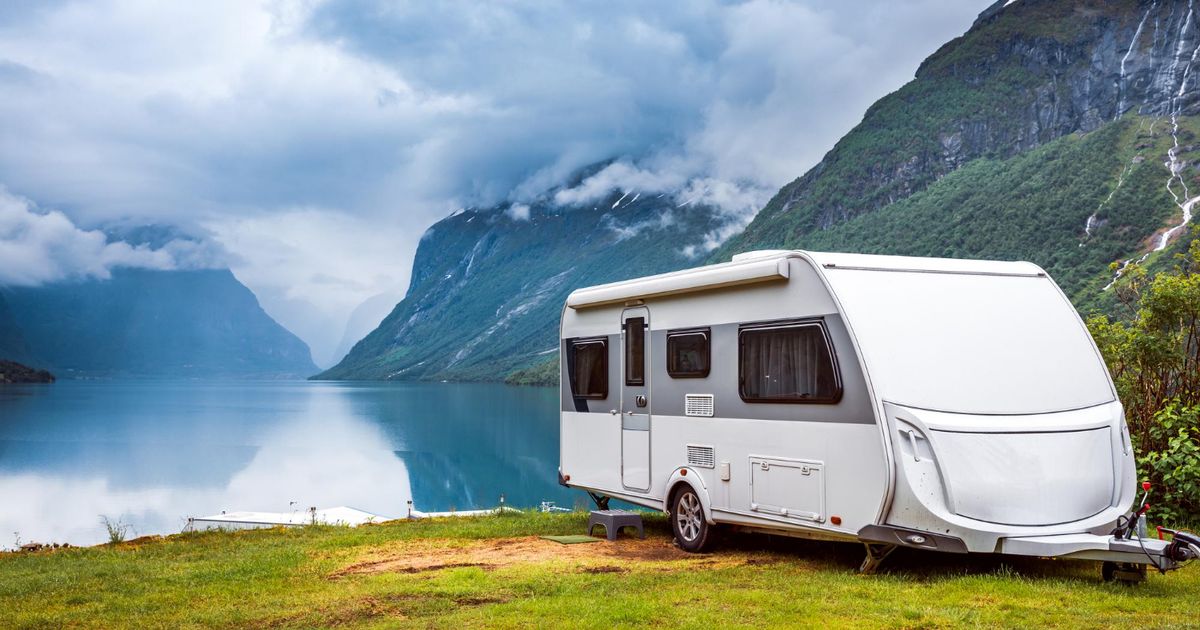 A white camper van in front of a lake with mountains