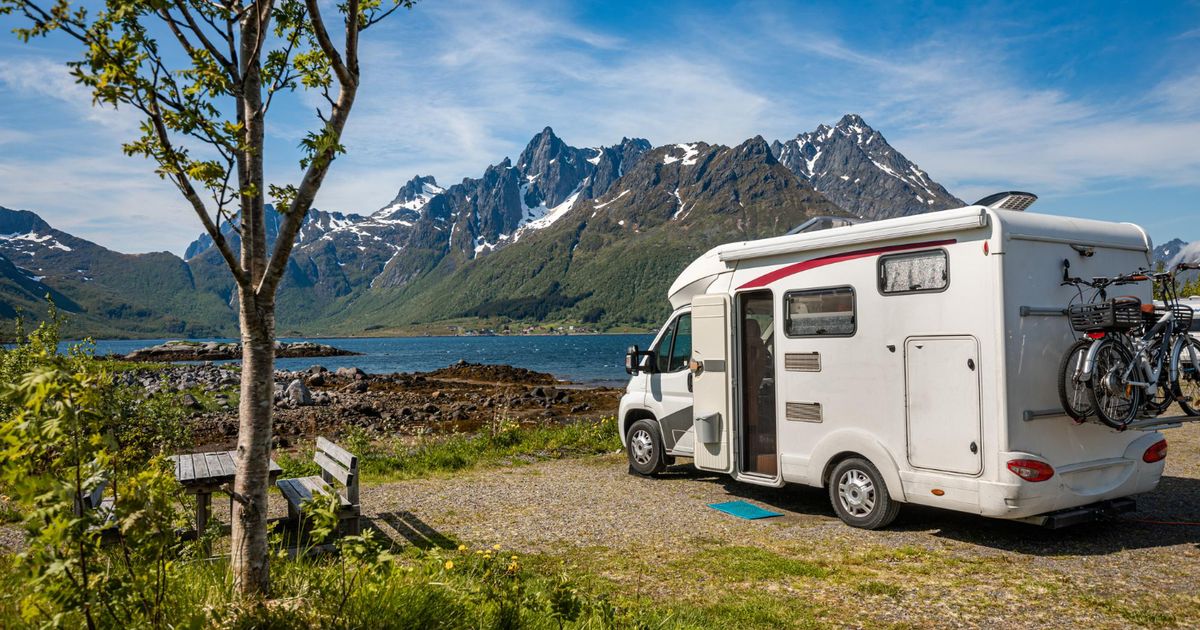 A white camper van in front of a lake with the mountains