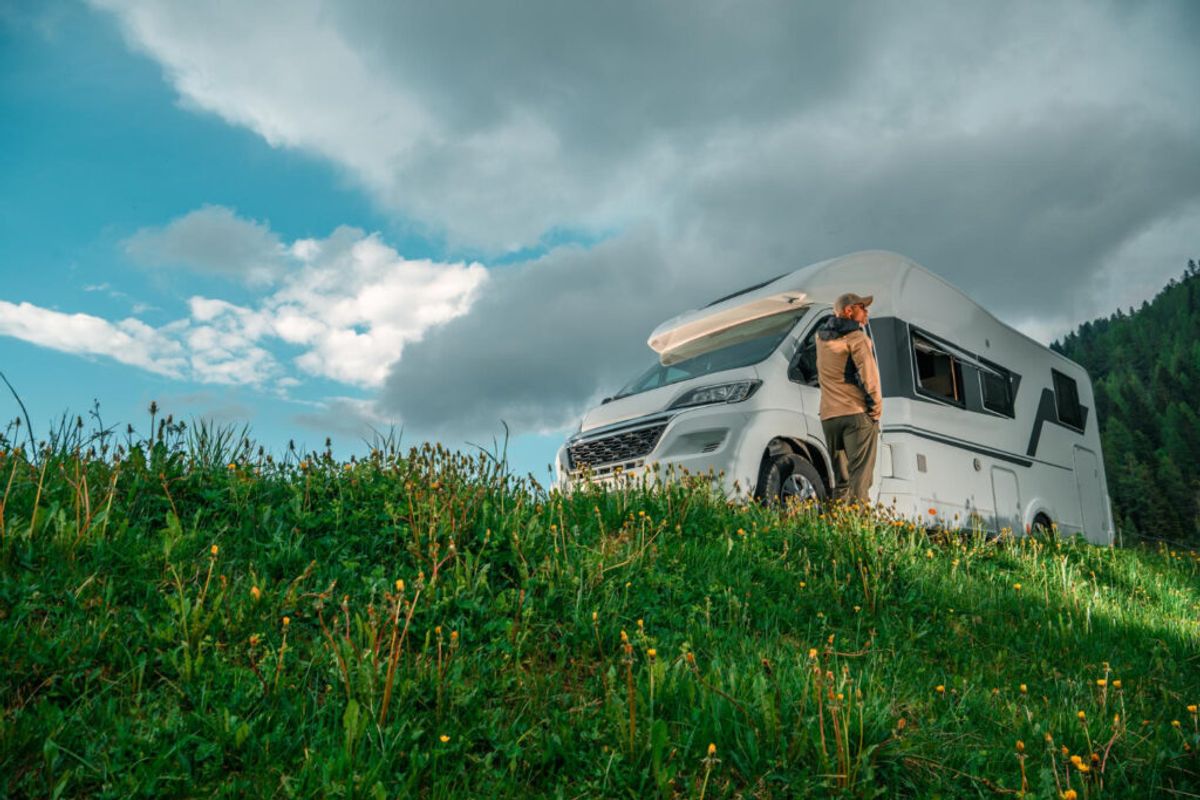 a man in front of his camper van in a low point of view with clouds and the green grass thanks to campground registration software