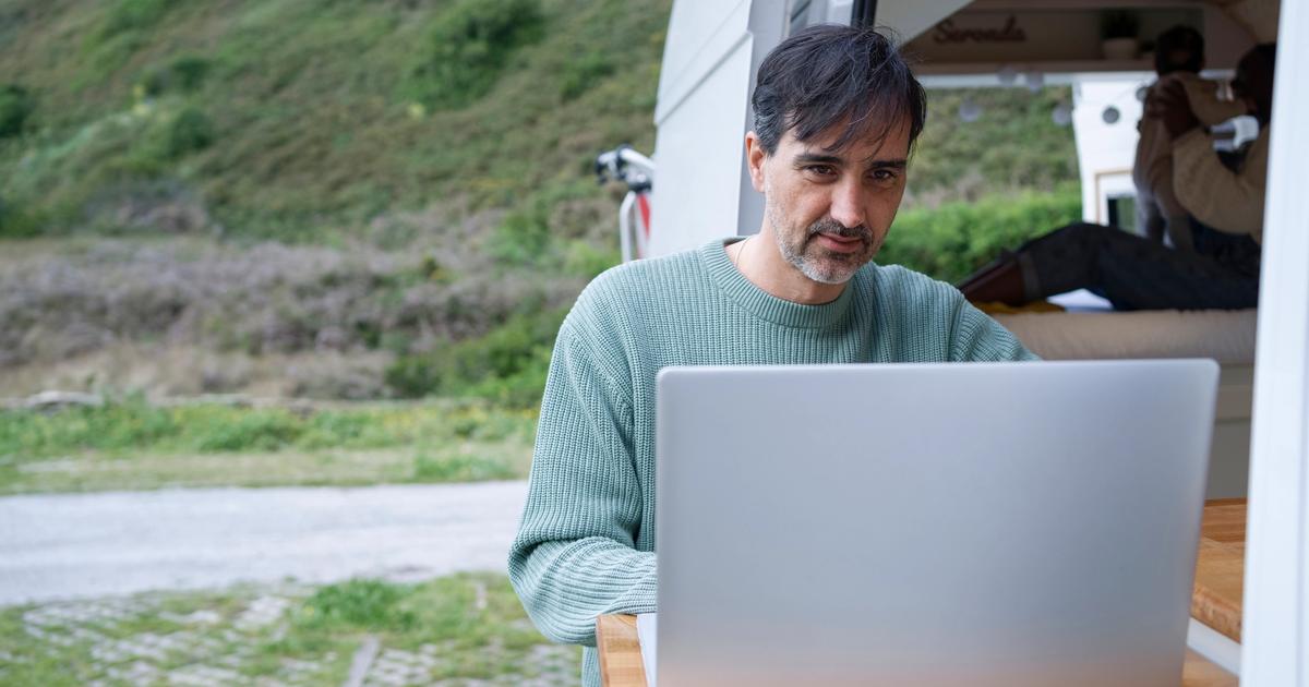 Man working on laptop outside an RV camper van with hillside landscape in background