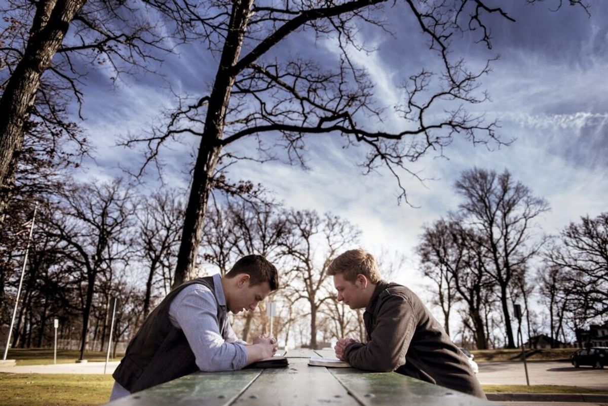 Two men sitting at opposite ends of a picnic table in a bare winter park, reviewing documents together outdoors.