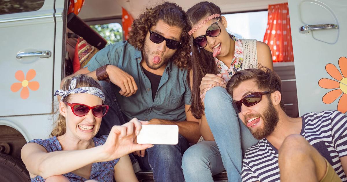 Group of young adults taking a selfie inside a retro camper van, wearing sunglasses and smiling at the camera.