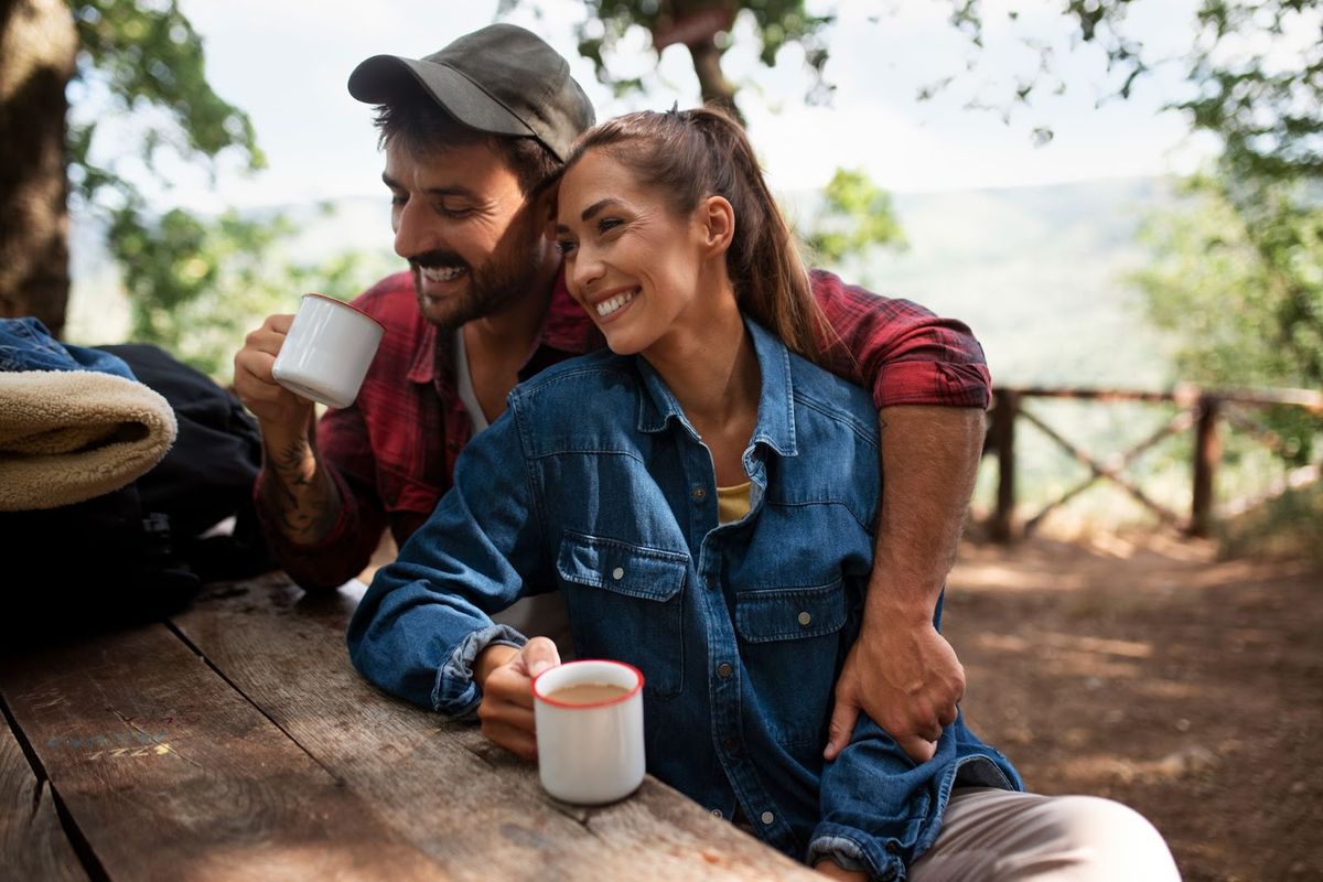 Couple enjoying coffee together at a rustic wooden table overlooking a scenic valley landscape at an RV campground.