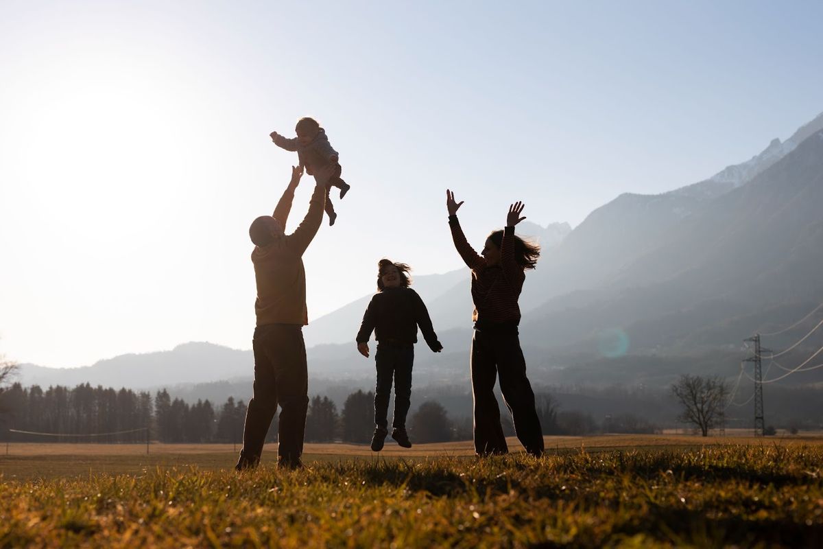 Family of four playing joyfully in an open field with misty mountains in the background during golden hour.