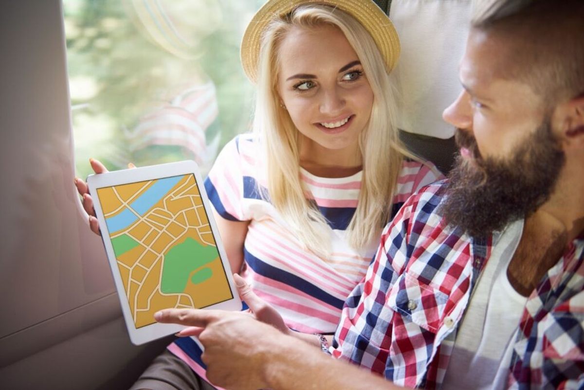 Woman showing a bearded man a street map on a tablet while riding in a vehicle