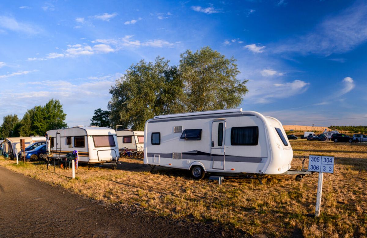 Row of parked caravans at a sunny campsite with numbered plot markers, trees, and open fields under blue sky.