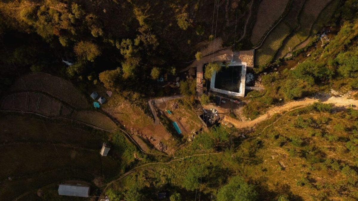 Aerial view of a rustic campsite nestled in dense forest with cabins, cleared pathways, and overgrown vegetation surrounding the property.