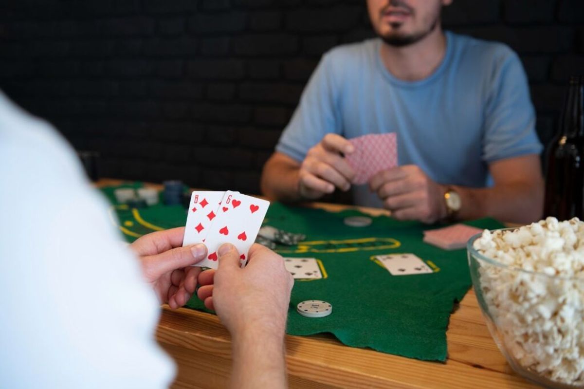 Two people playing poker at a green felt table with cards, poker chips, and popcorn during a casual game.