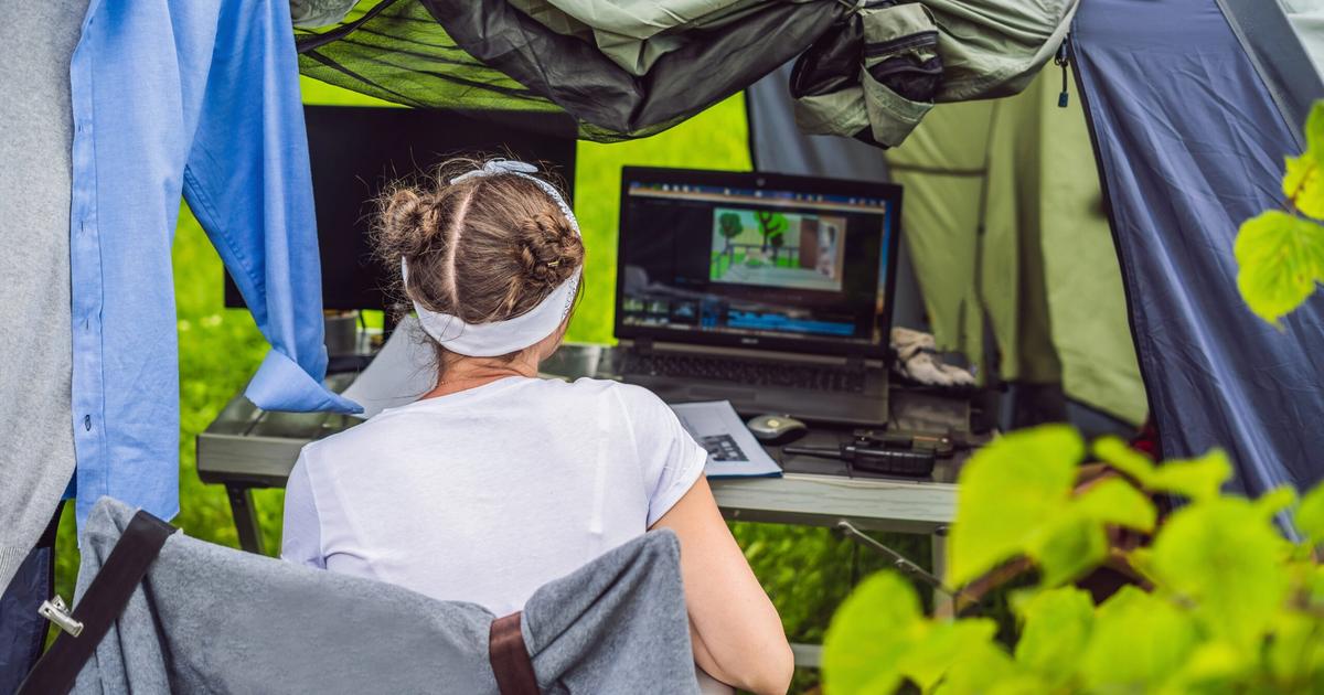 Person working on campground design software on laptop inside a tent, surrounded by green foliage and outdoor camping setup.