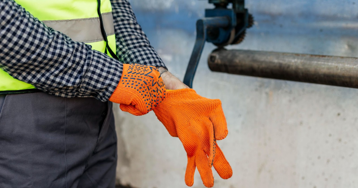 Worker in safety vest and orange grip gloves holding concrete barrier at RV park construction site with camera equipment visible.