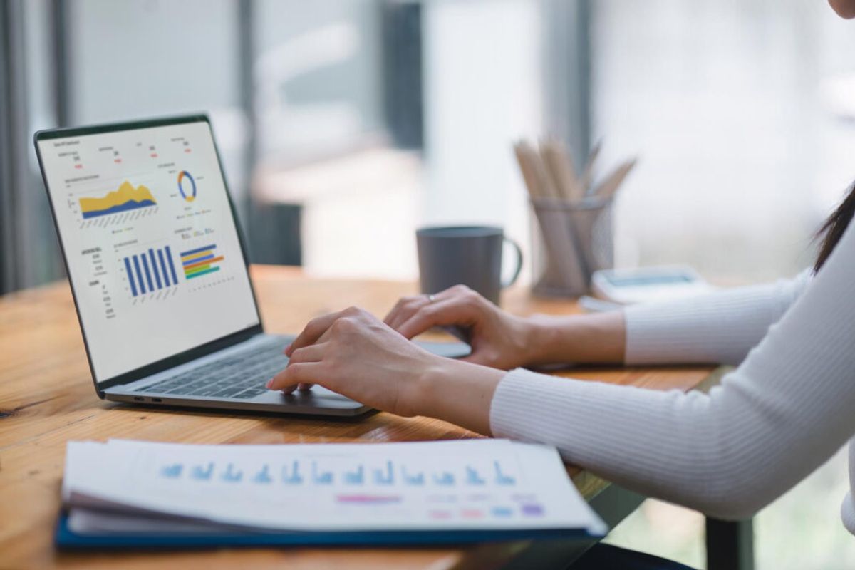 a person in a white sueter checking her laptop to see the analitycs and metrics of their campground using management software 